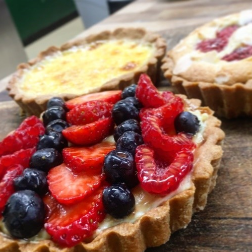 Three sweet pastry tarts, the closest of which is filled with fresh fruit slices of raspberries, strawberries and blueberries